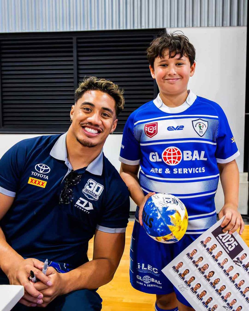 Male Ruby player smiling next to junior ruby player holding signed ball and poster