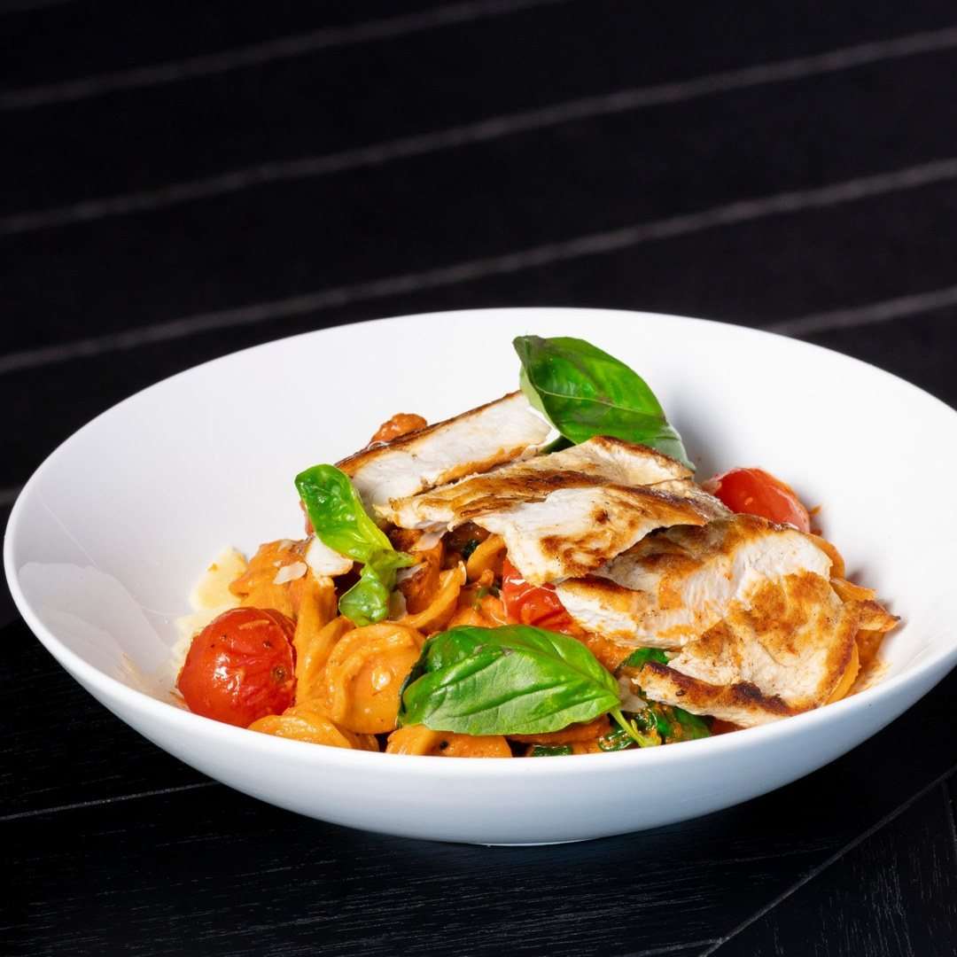 Grilled chicken served over creamy tomato pasta with cherry tomatoes and fresh basil at Conservatory, Fuller Sports.